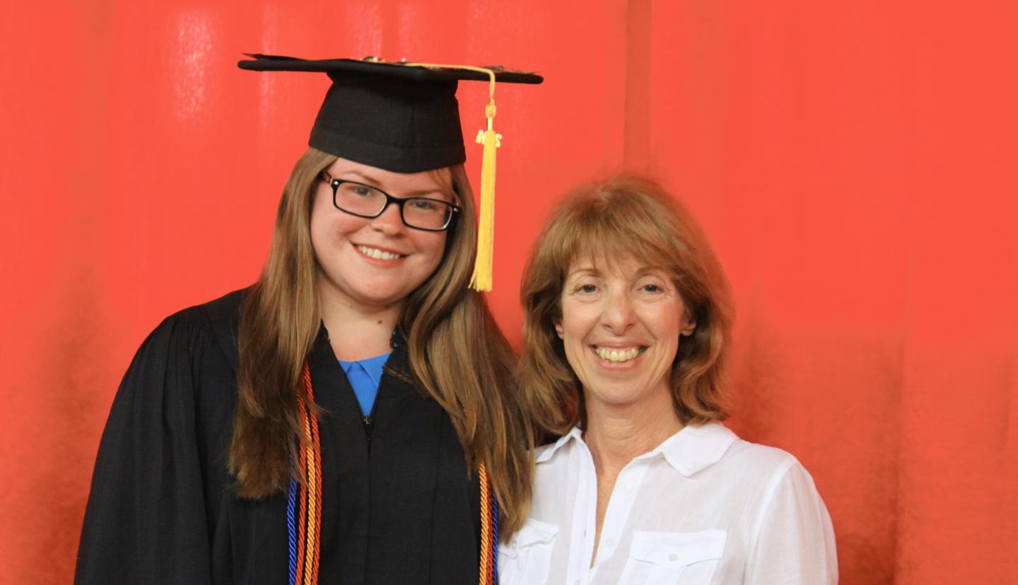 A young woman wearing a graduation cap and gown stands next to an older woman