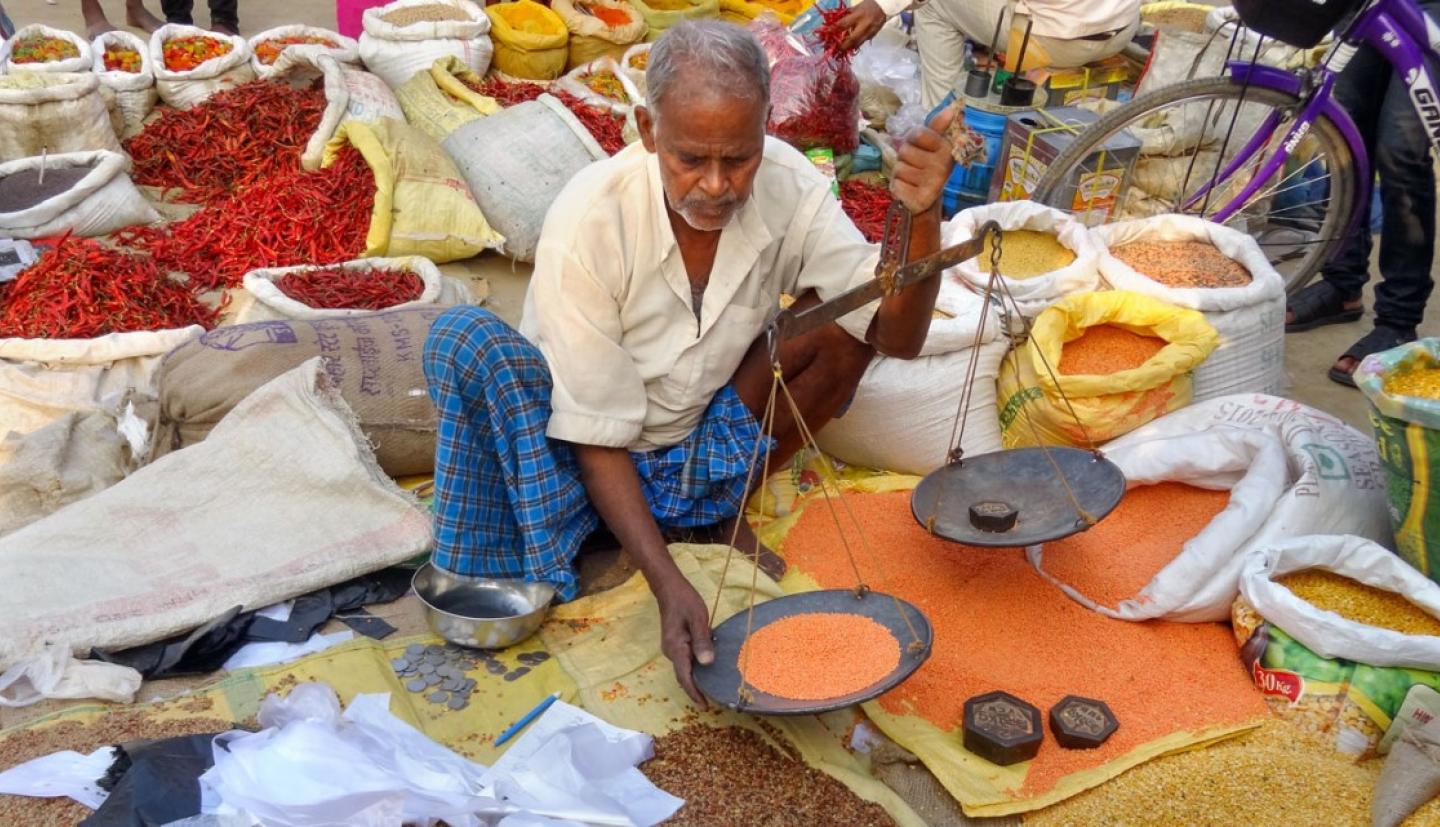 A man weighs different grains in an outdoor market.