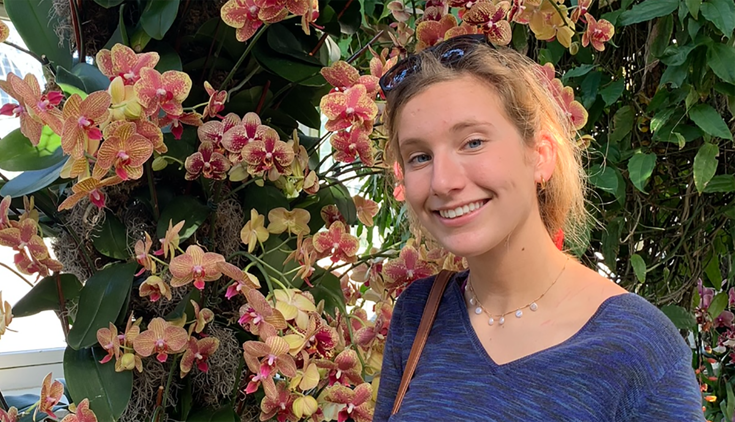 a student stands in front of blooming flowers