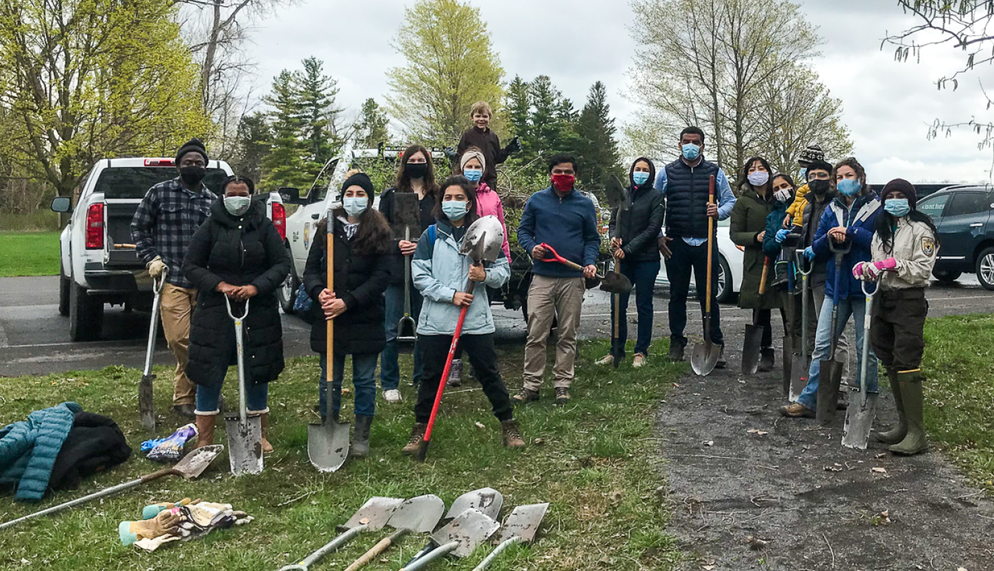 A group stands outside near a parking lot in a forested area 