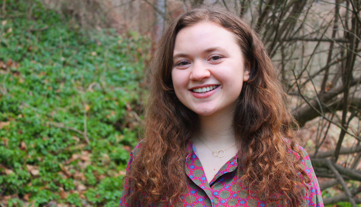 a student in a colorful shirt stands in front of a green hill