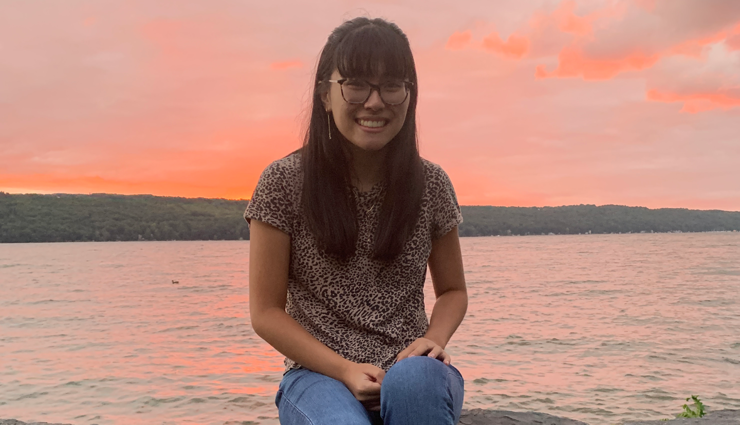 a student sits in front of water and an orange sky