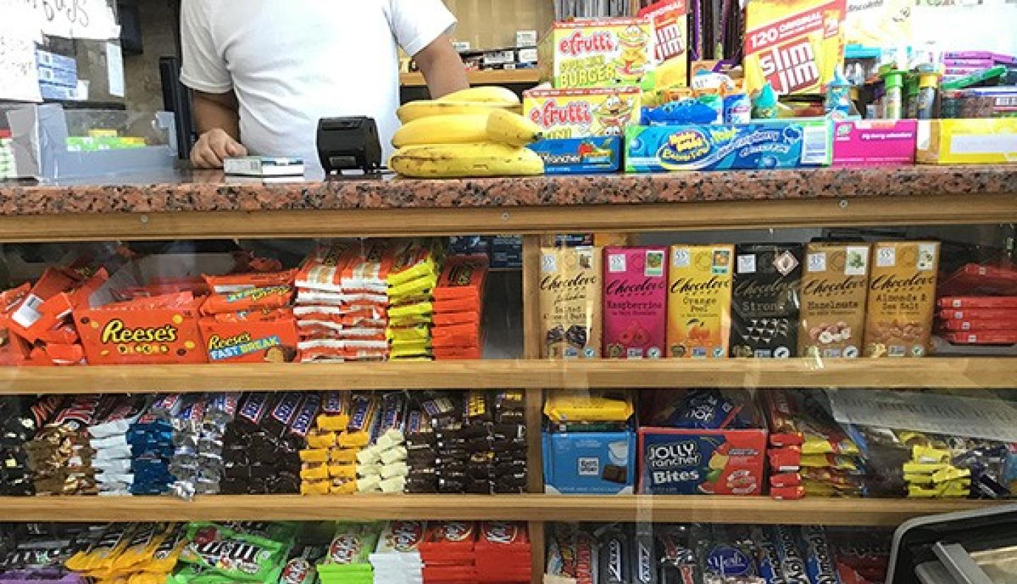Shelves in a bodega full of candy and snacks with just a few bananas on the counter.