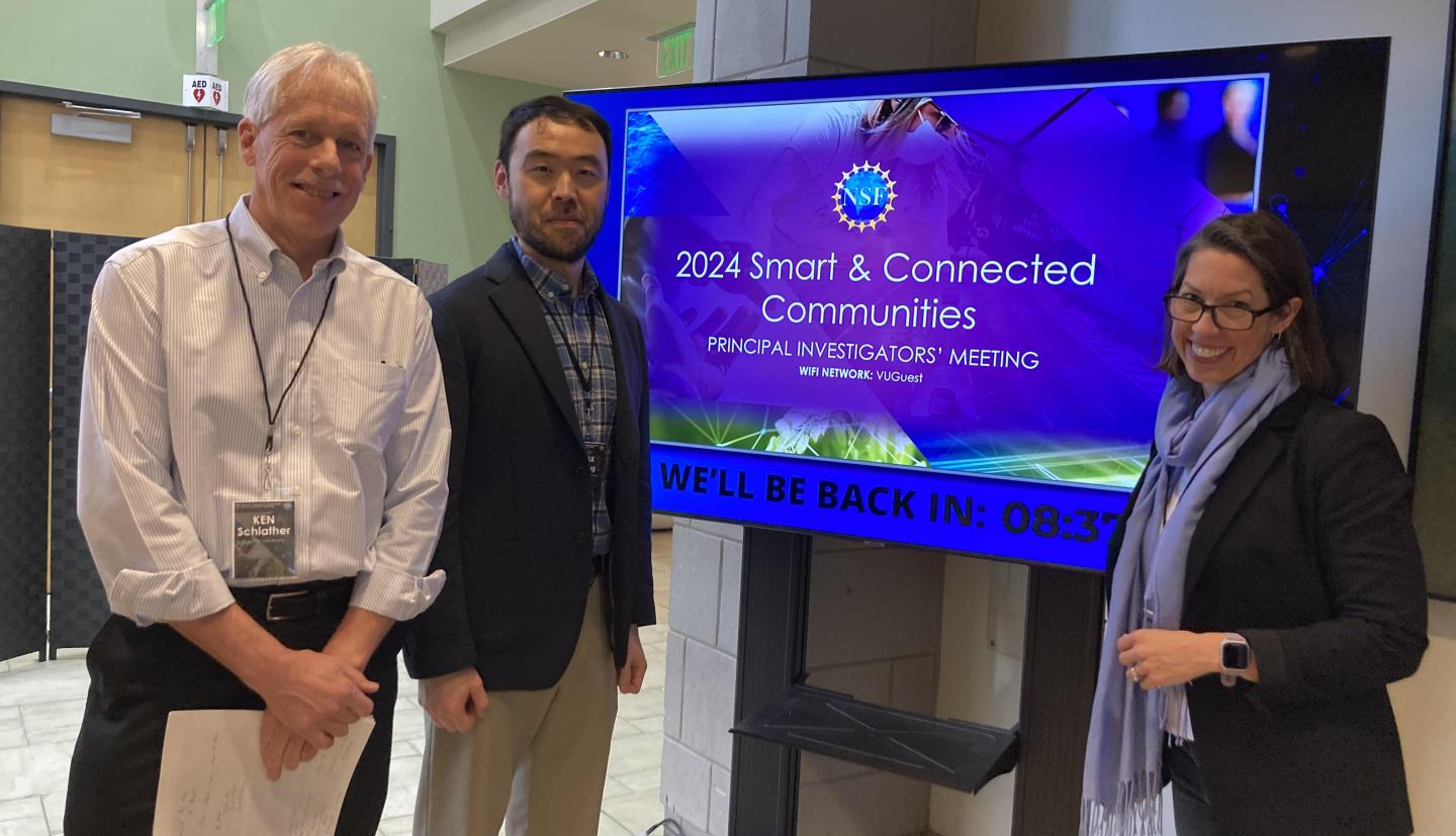 3 people stand in front of TV screen smiling