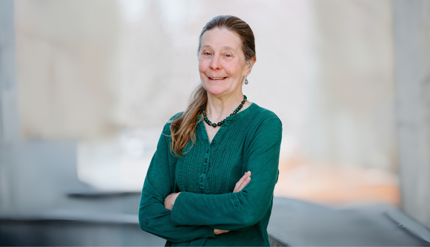 Margaret stands with arms crossed in a stone courtyard.