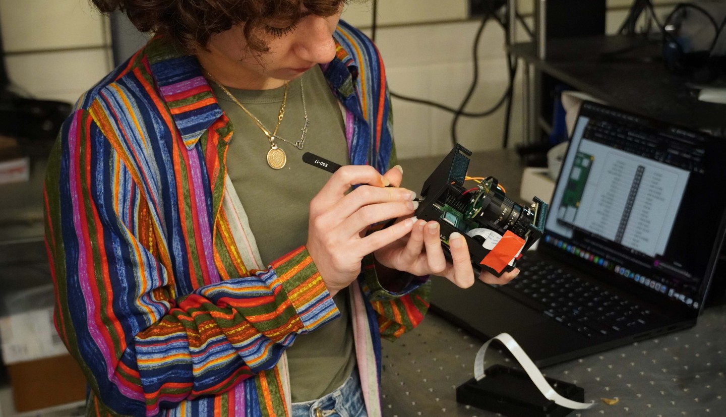 a woman holds a piece of tech and works on it with a tool