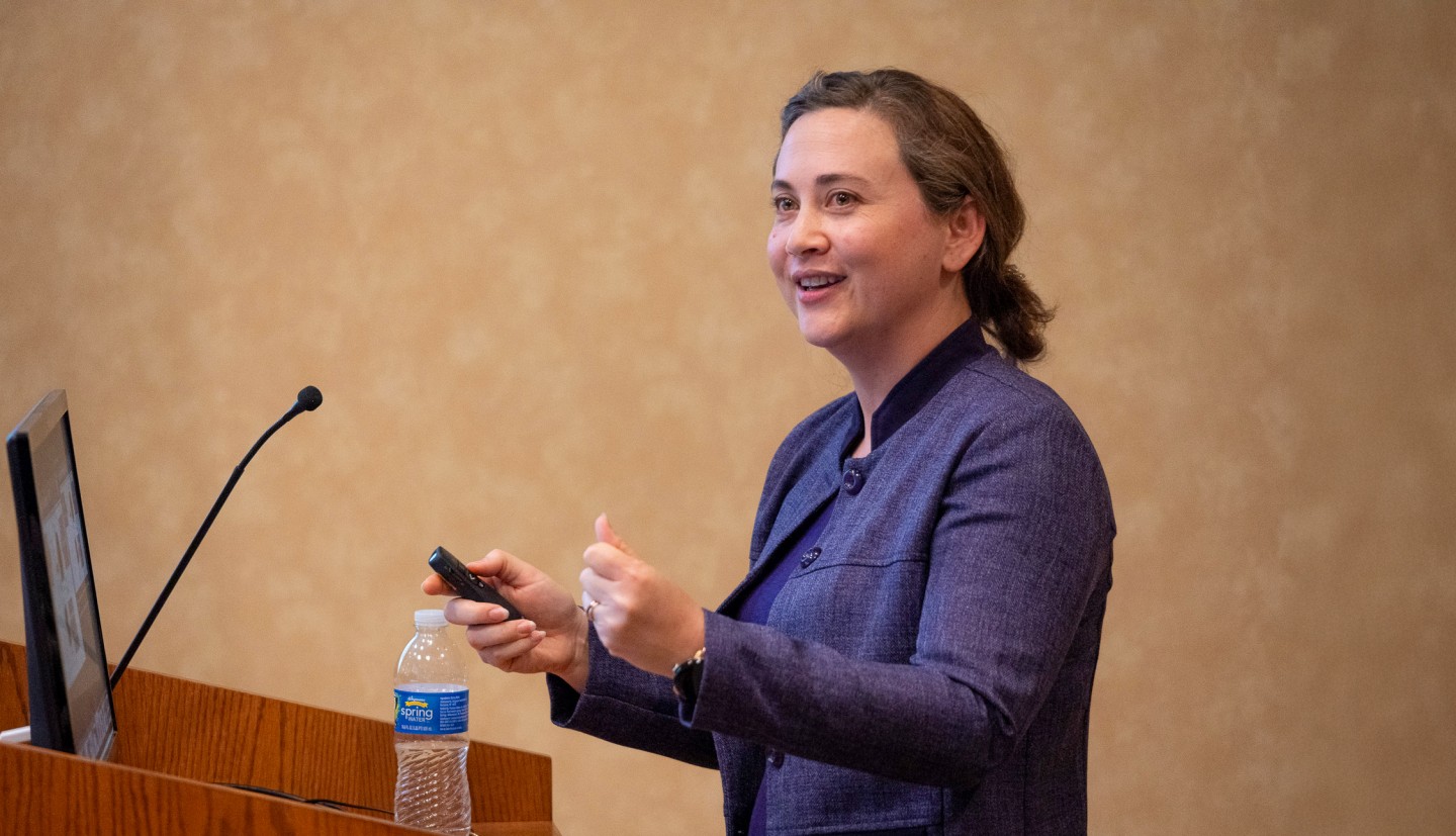 a woman stands behind a podium, speaking