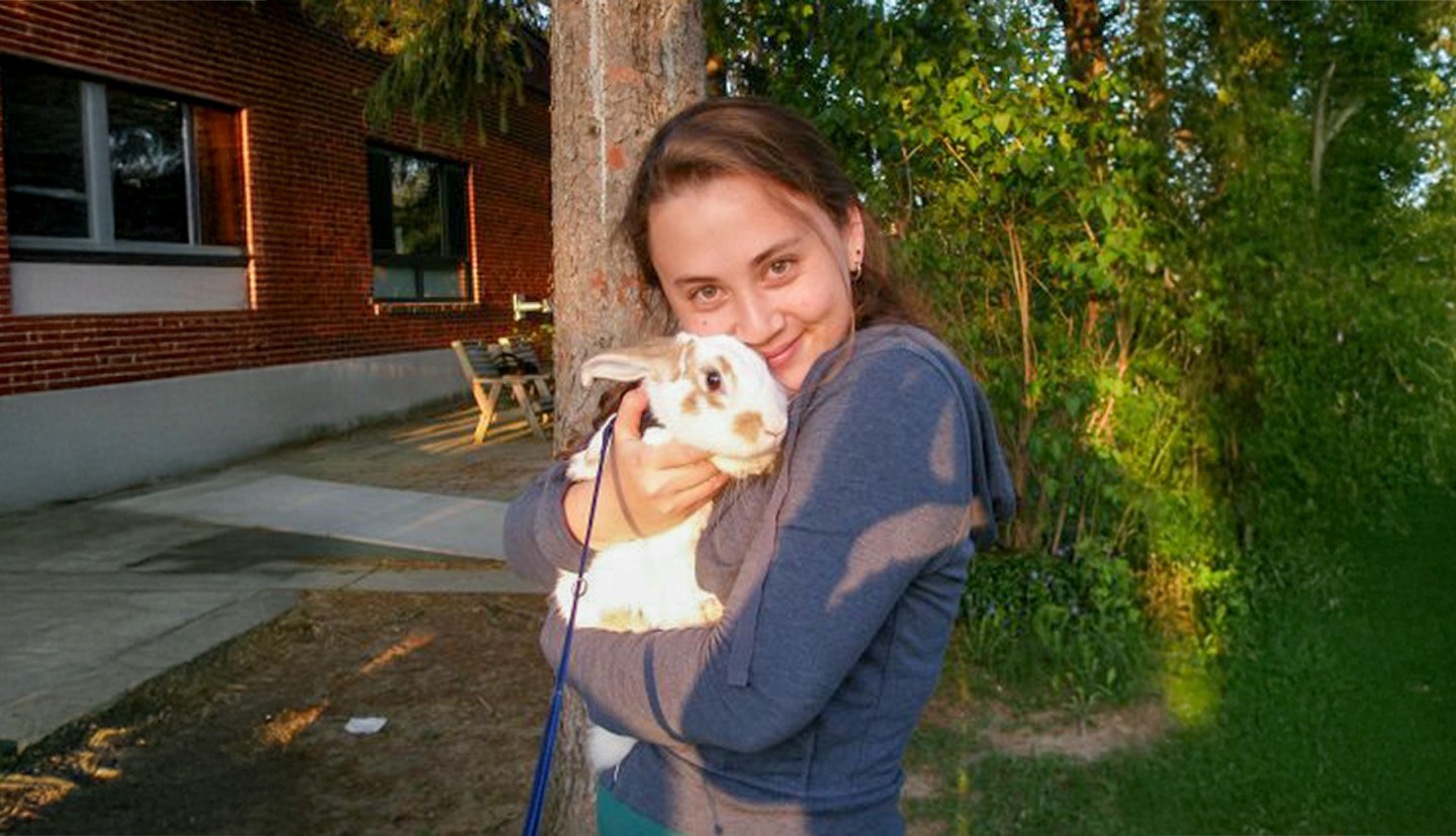 a woman stands outside, holding a rabbit