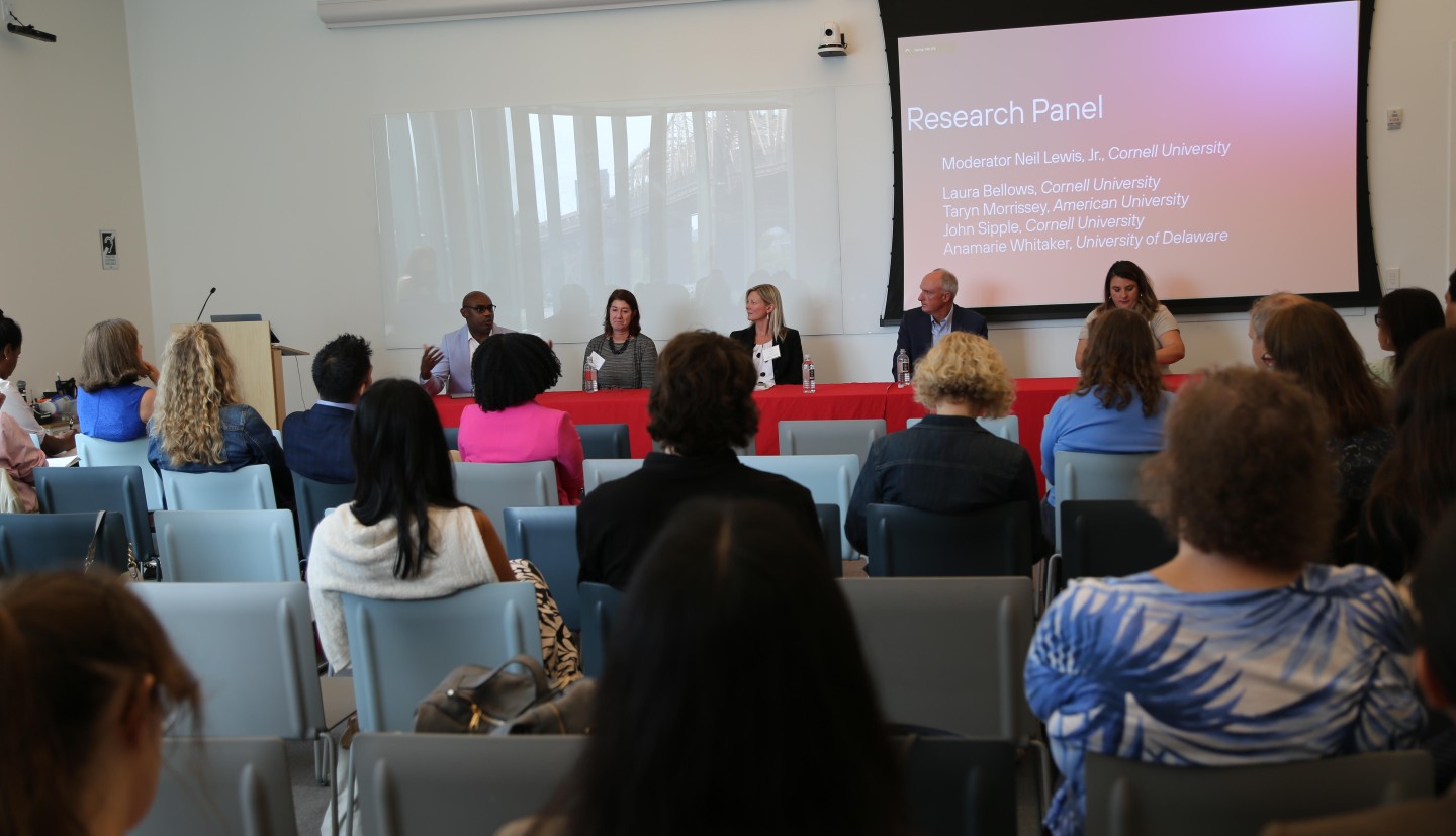 5 individuals sit in the front of room having research panel