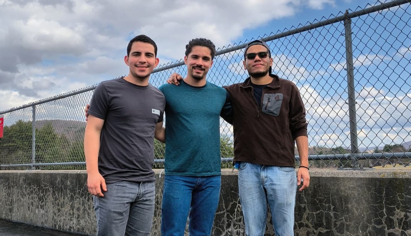 Three men pose together on a bridge.
