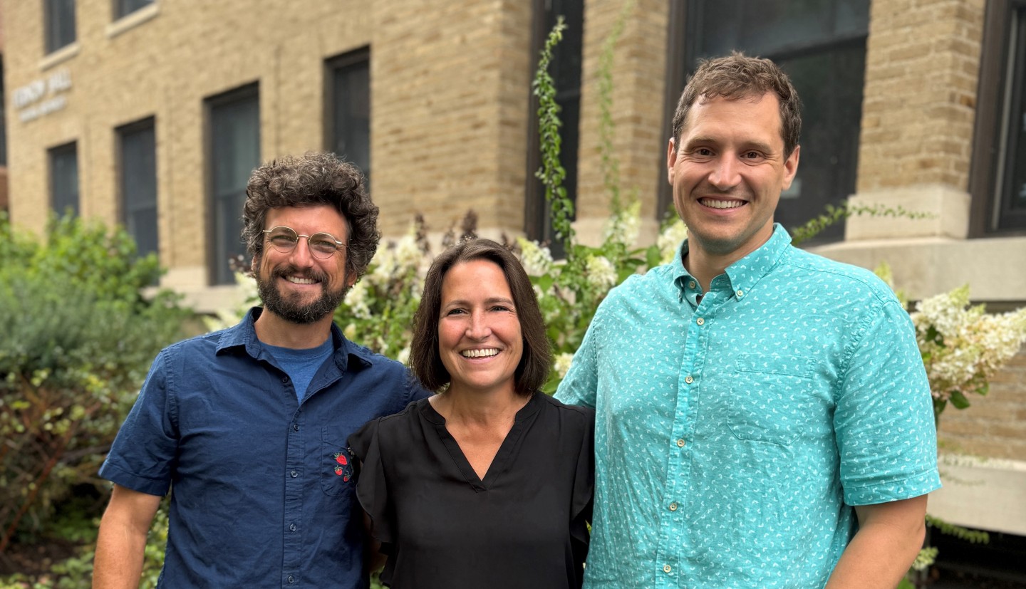 Three people stand together smiling at the camera