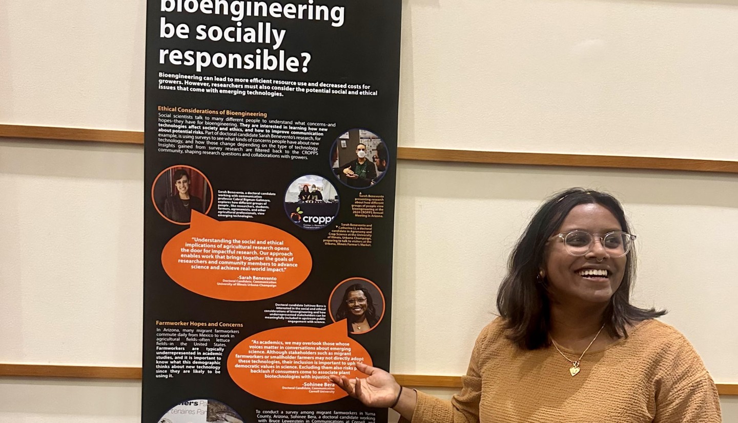 person standing in front of banner, pointing to it