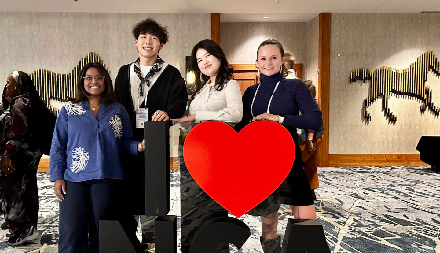 four people stand in front of a sign that reads I heart NCA