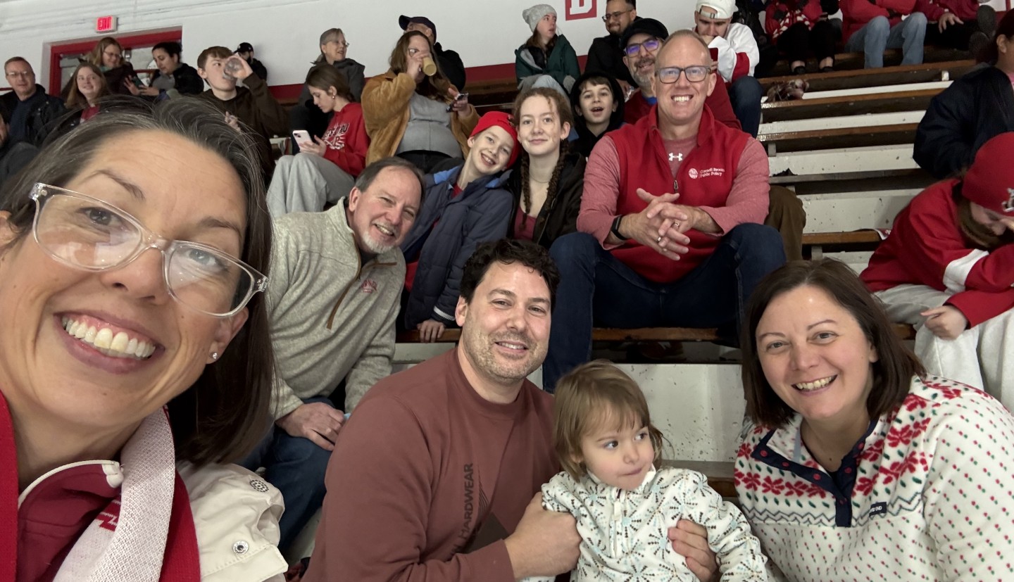 cornell comm staff pose for a selfie with their children in the stands of the hockey game 