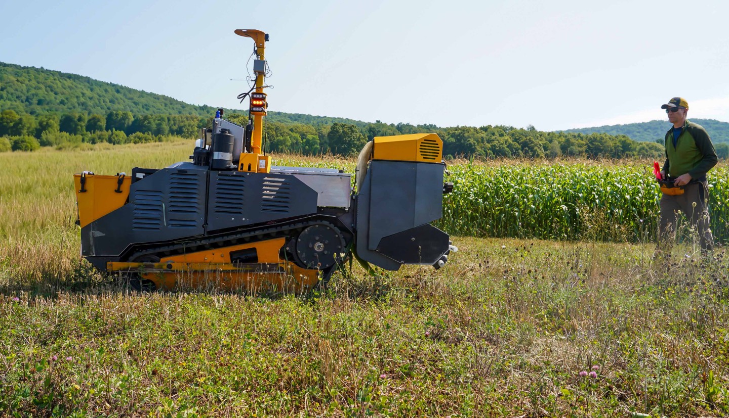 an autonomous tractor rolls over a field with a man walking behind it