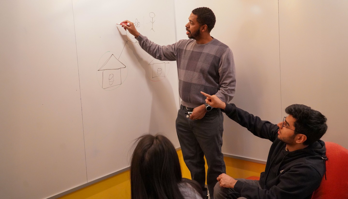 a man writes on a whiteboard while another man points at what he's written