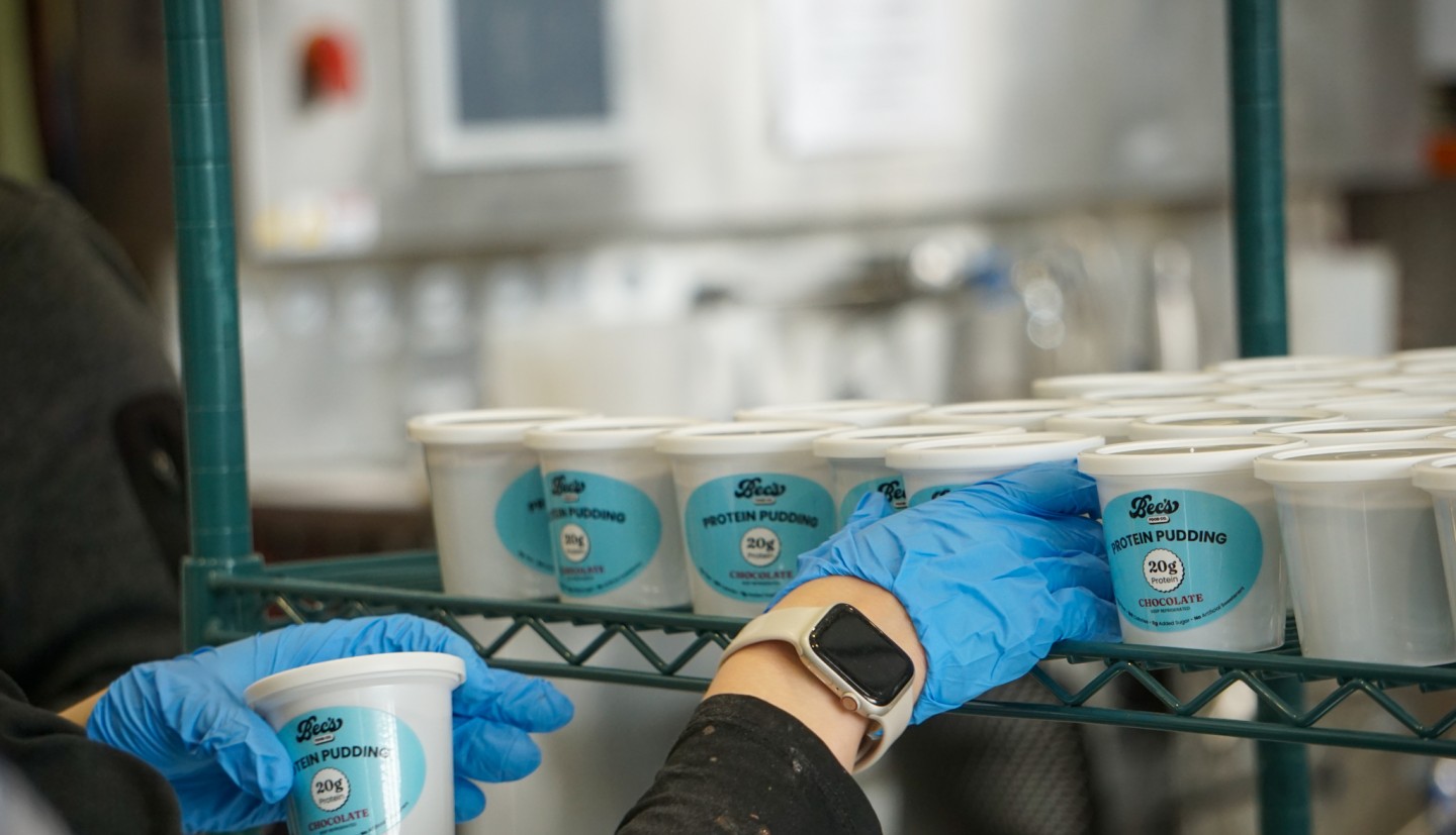 A person placing white plastic cups of pudding on a rack. 