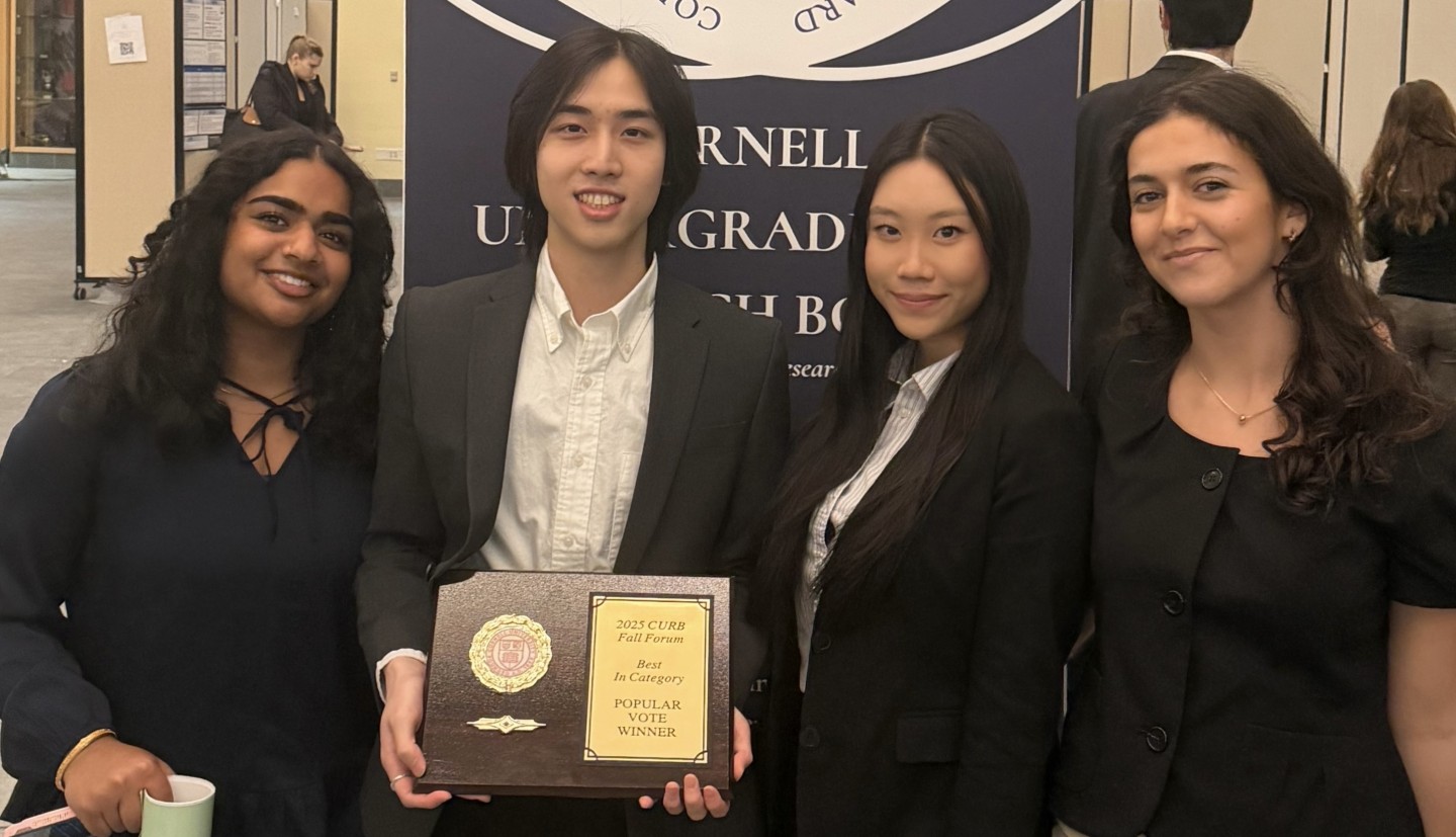 four students stand holding a plaque saying "peoples choice" in front of their poster