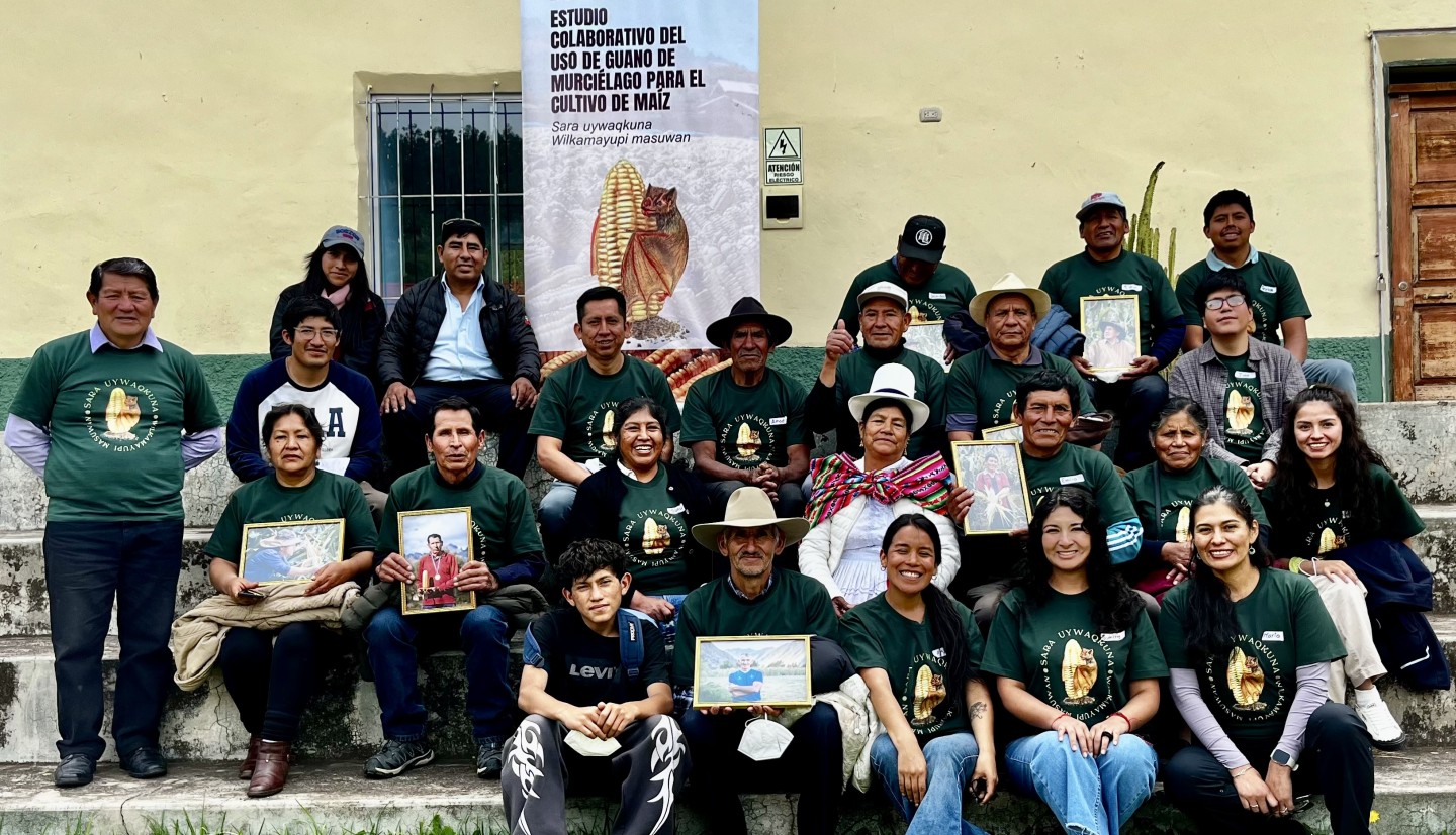 group of individuals smile for a picture in front of maize banner