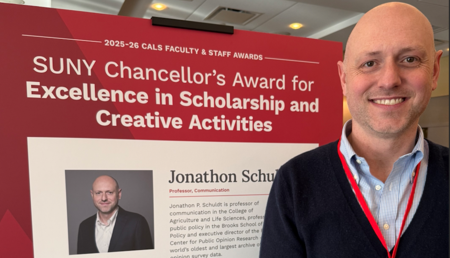 Jon Schuldt stands in front of SUNY Chancellor’s Award poster
