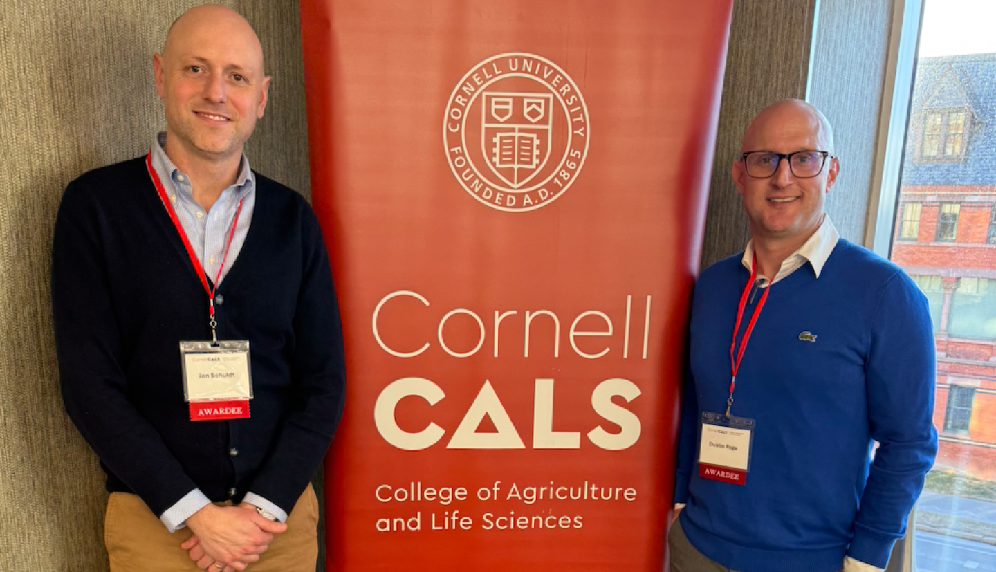 Dustin and Jon stand in front of Cornell CALS poster