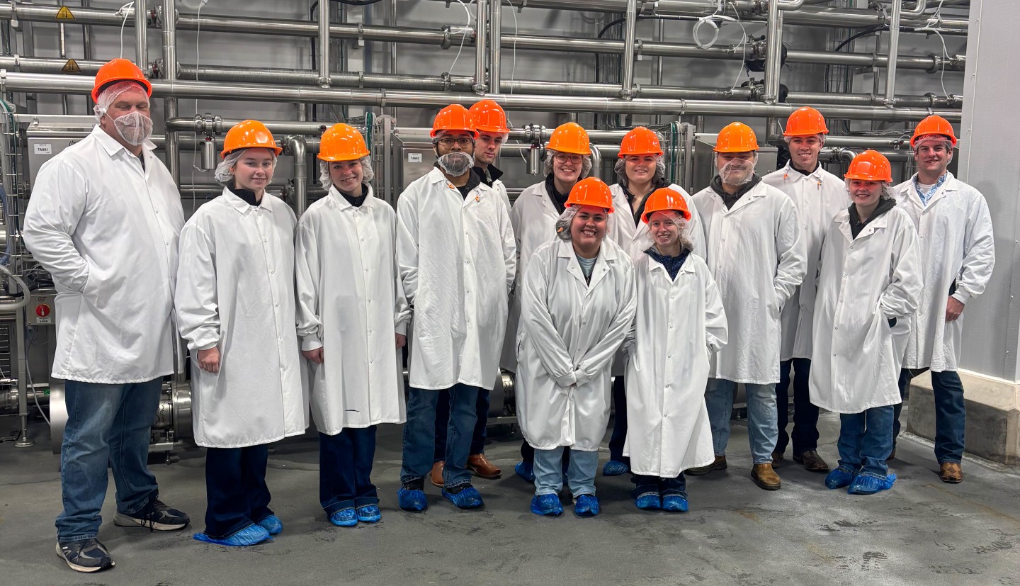 a group of people stand together wearing lab coats and hard hats