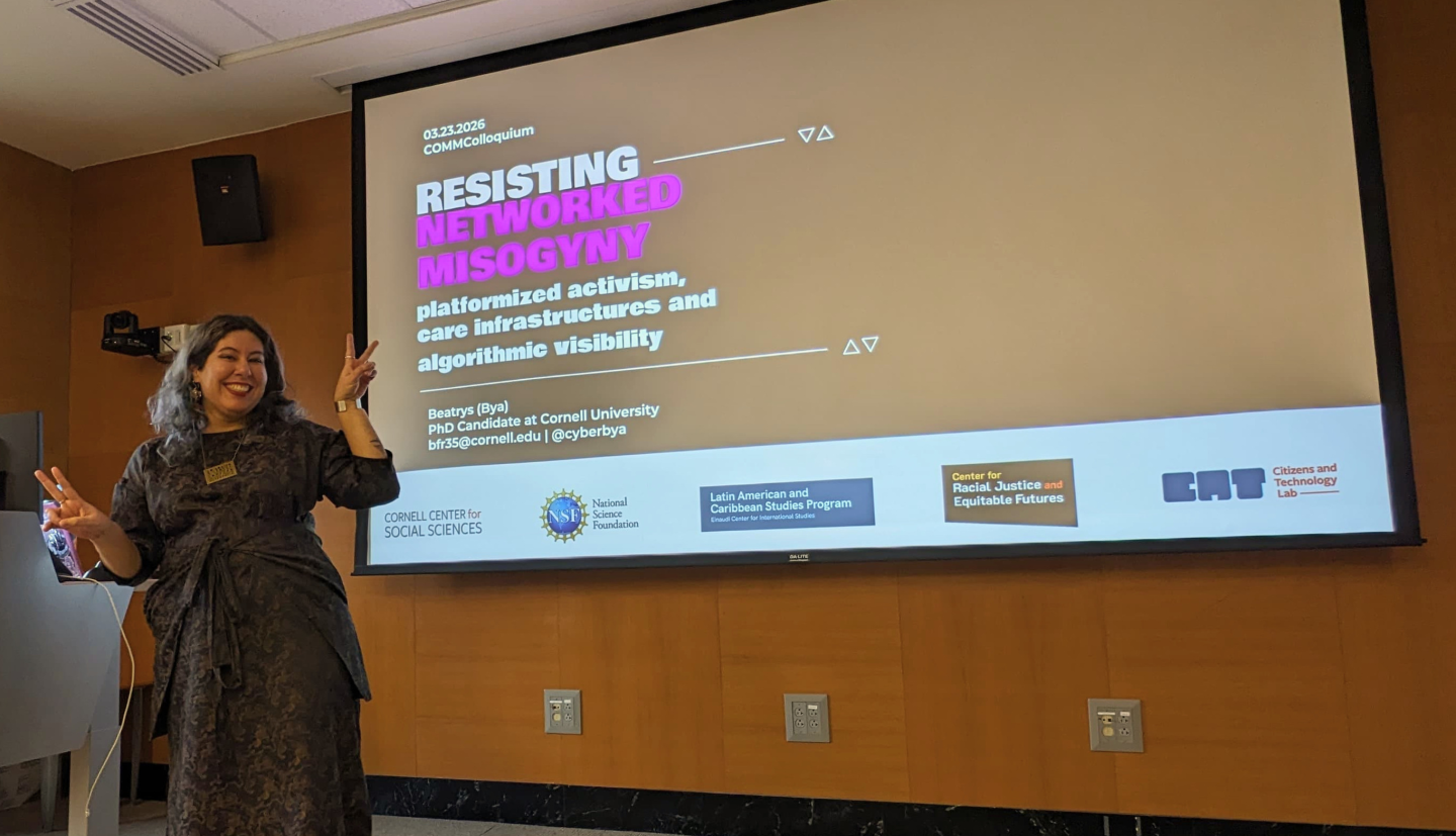 Beatrys Rodrigues presents on a stage in front of a screen