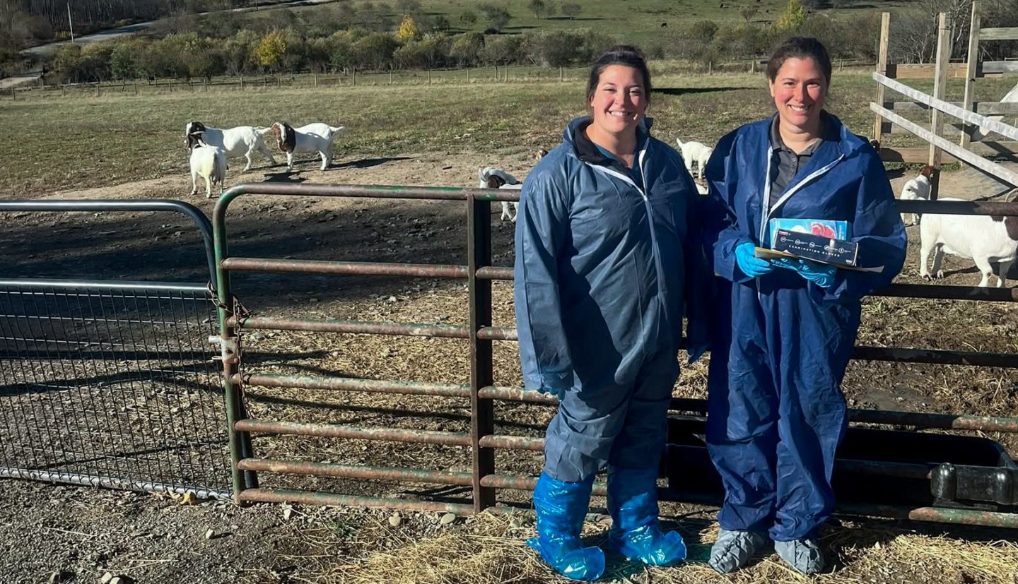 two women stand in front of a goat pasture