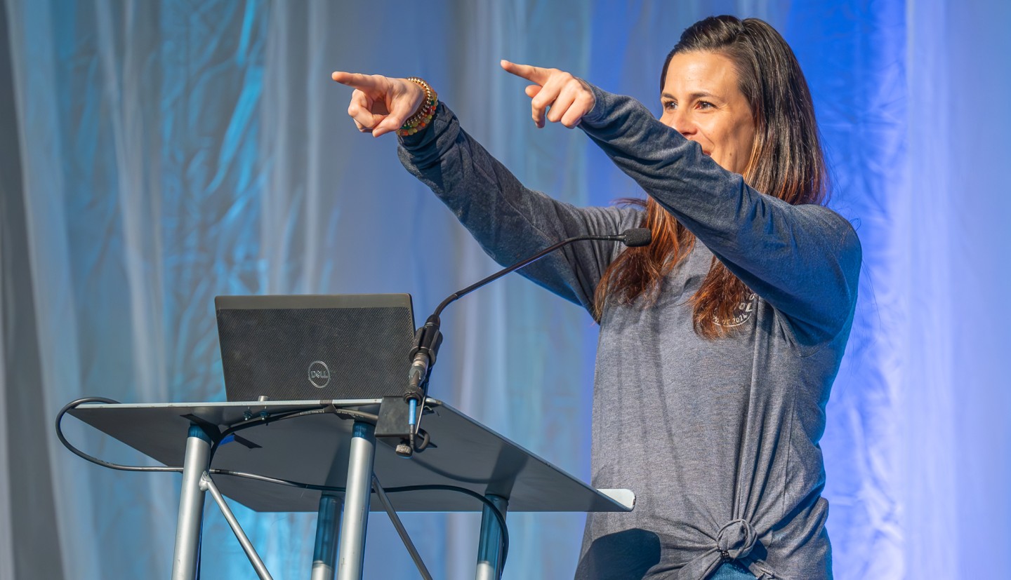 Cheryl with two arms raised pointing, during a talk at the 2024 farm to school summit.
