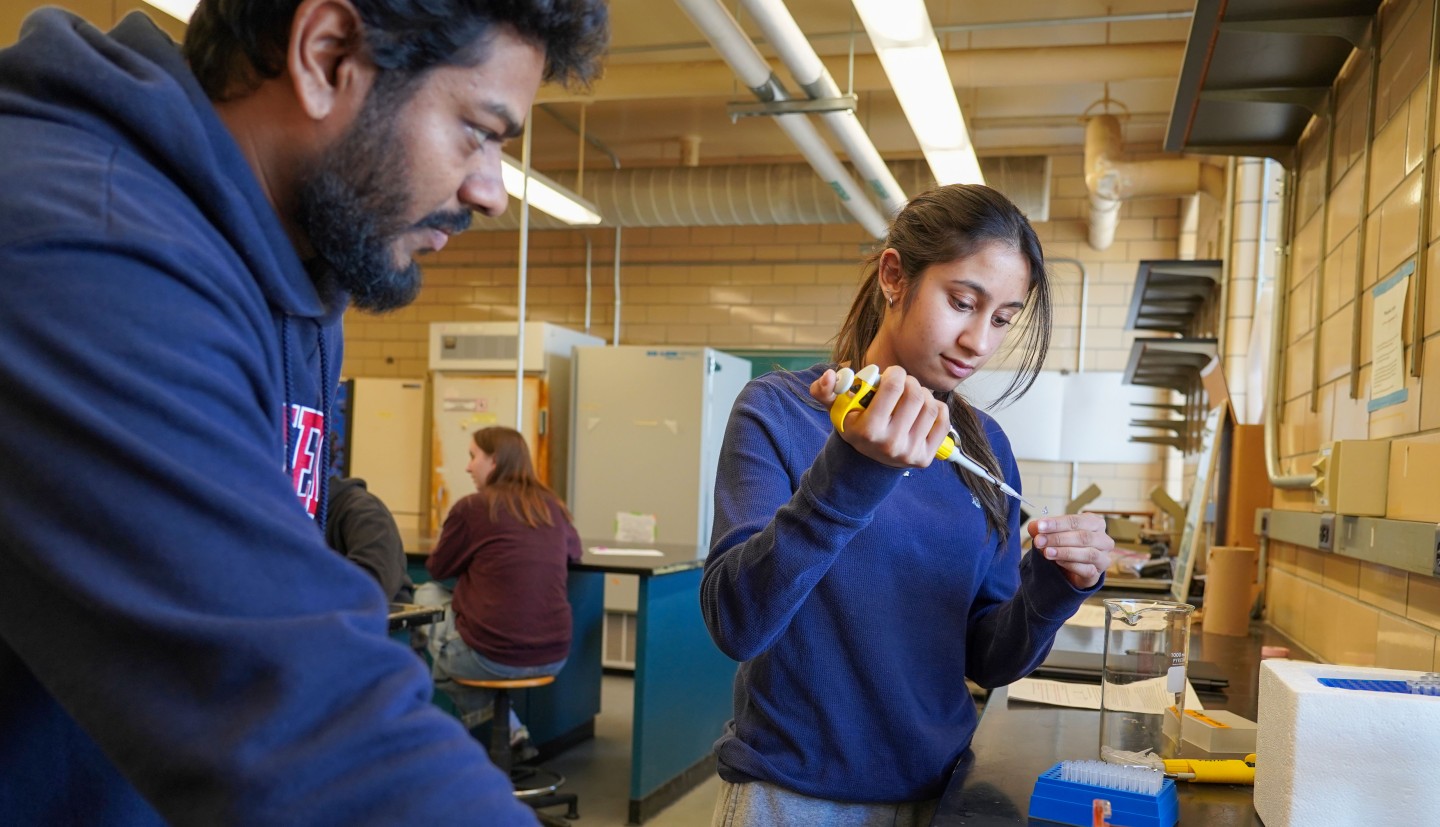 a man watches while a woman uses a pipette to measure out liquid