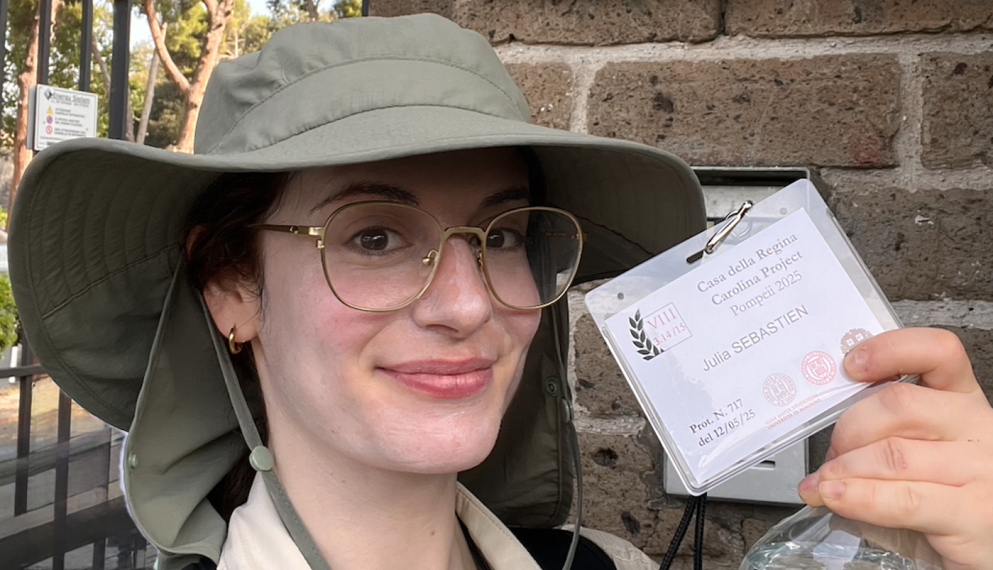 Julia Sebastien standing in front of archaeological site holding a badge