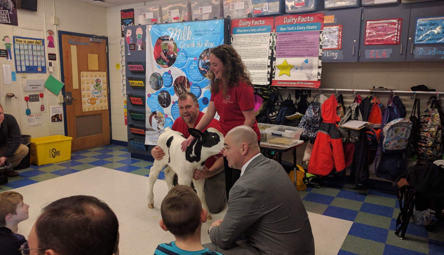 Brian holds a calf in front of a classroom while kids look on.