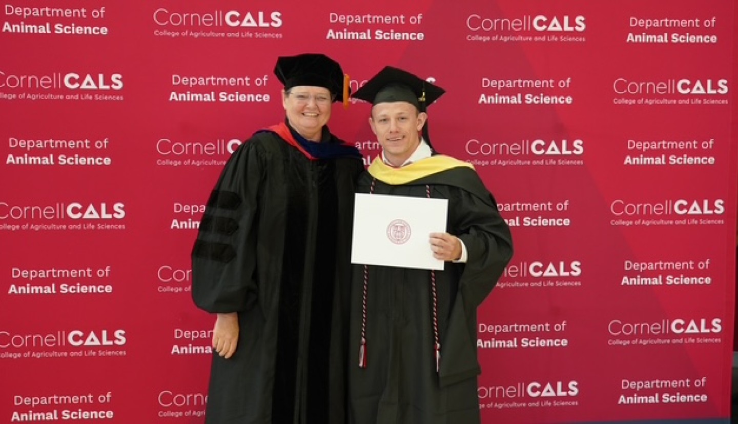 A woman (left) and a man (right) smile, dressed in graduation clothing.