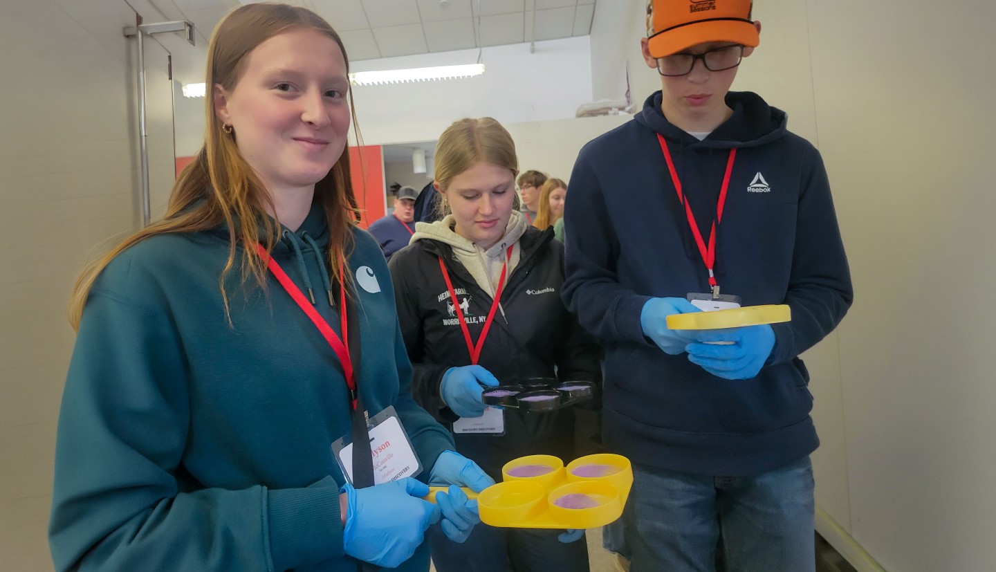 two girls and a boy stand holding containers with liquid in them