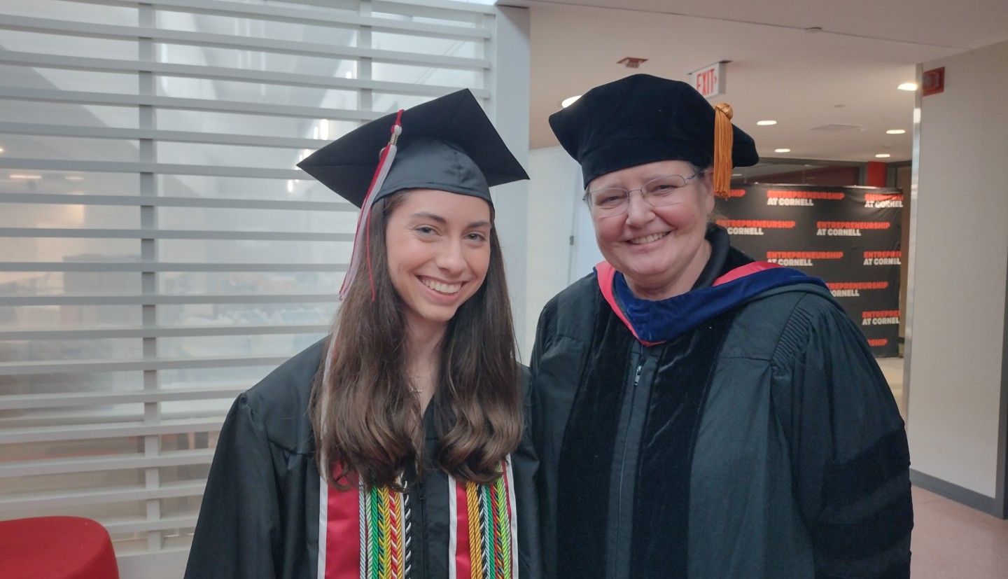 Two women wearing graduation clothing standing next to each other and smiling.