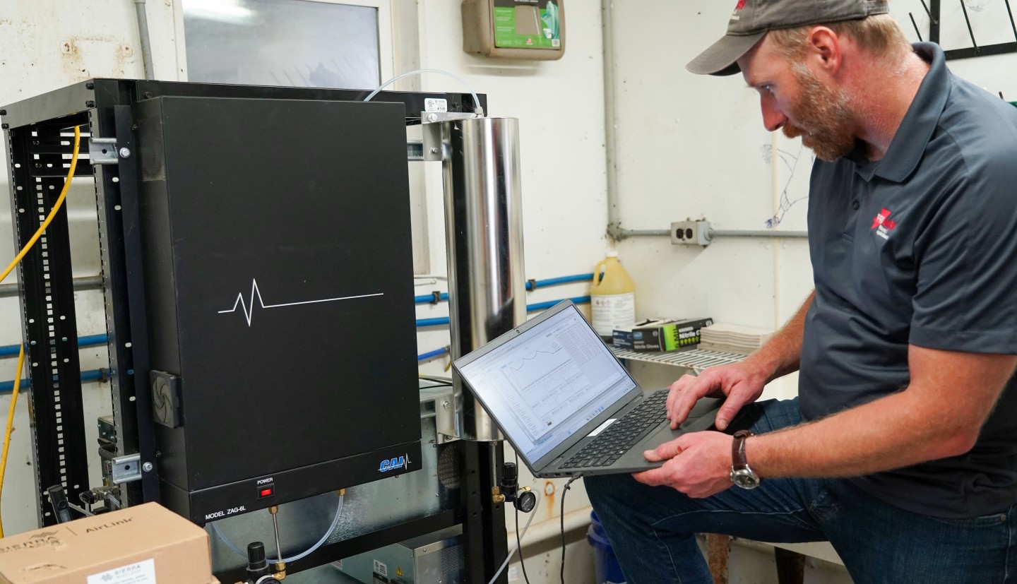 a man uses a laptop to look at data from a piece of tech in a farm shed