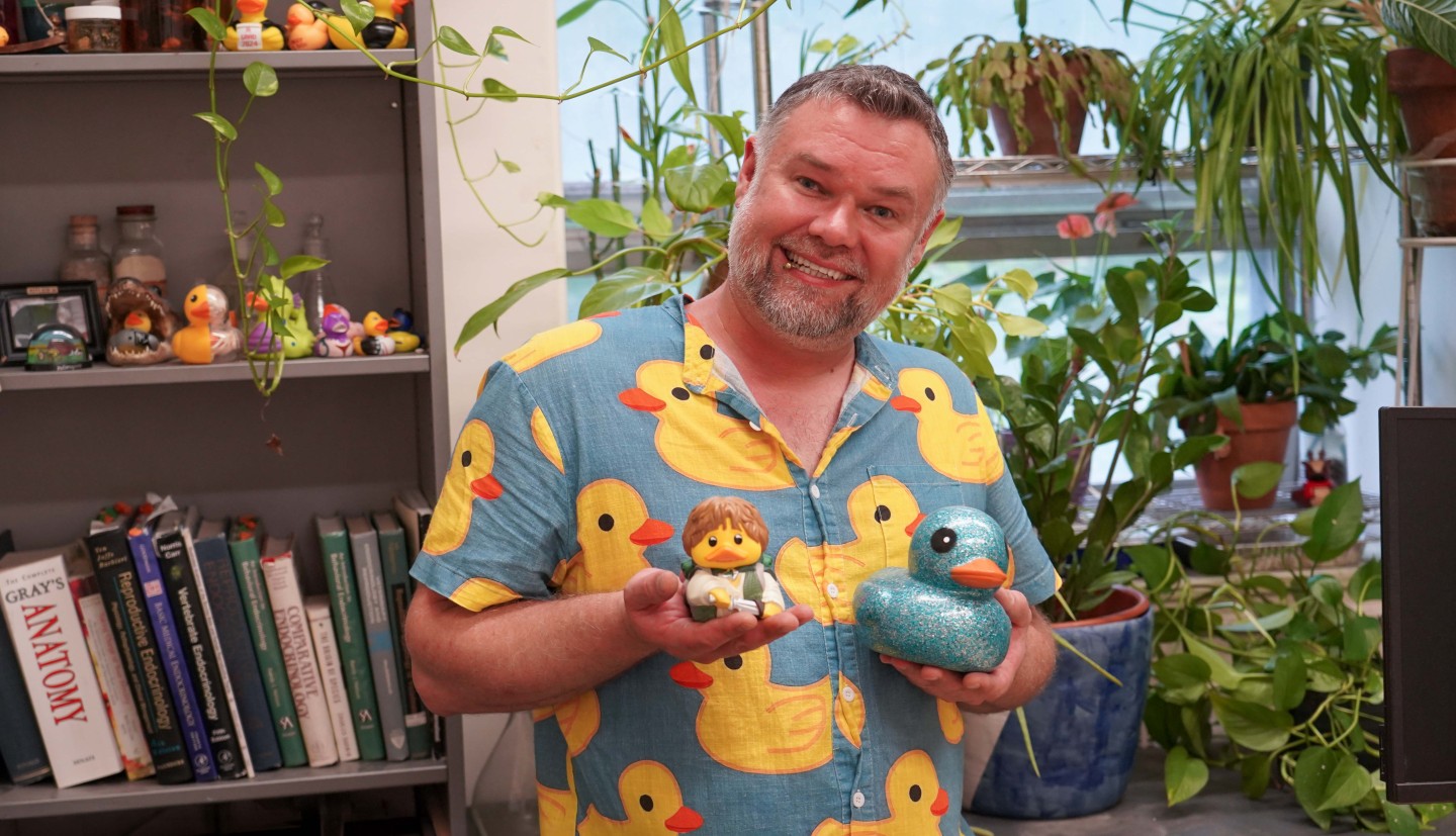 a man stands holding two rubber duckies.