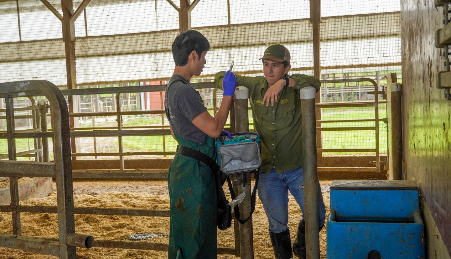 A man shows another man a vial of blood in a barn.