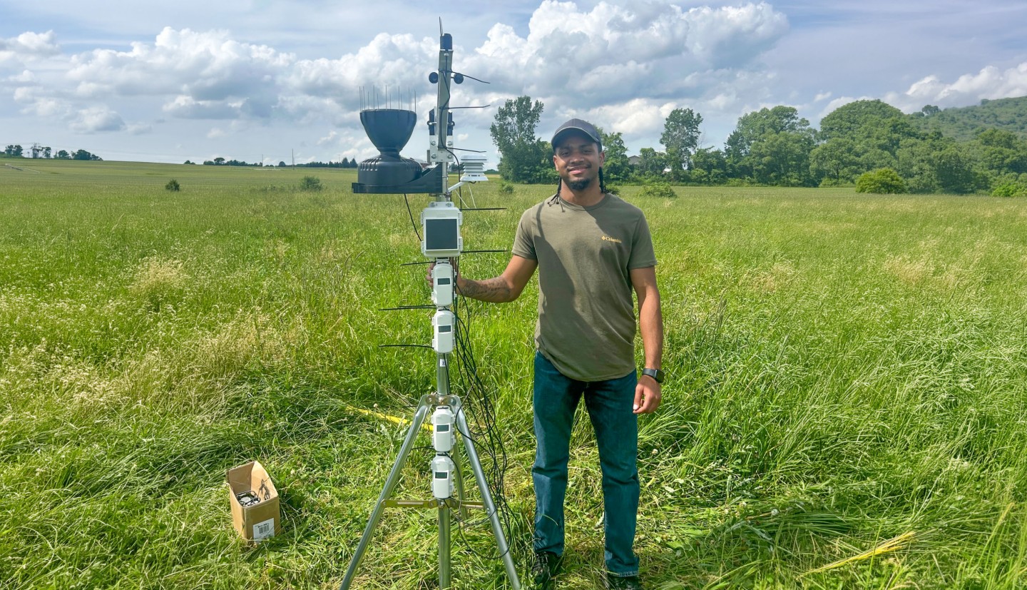 A man stands in a field next to a piece of tech