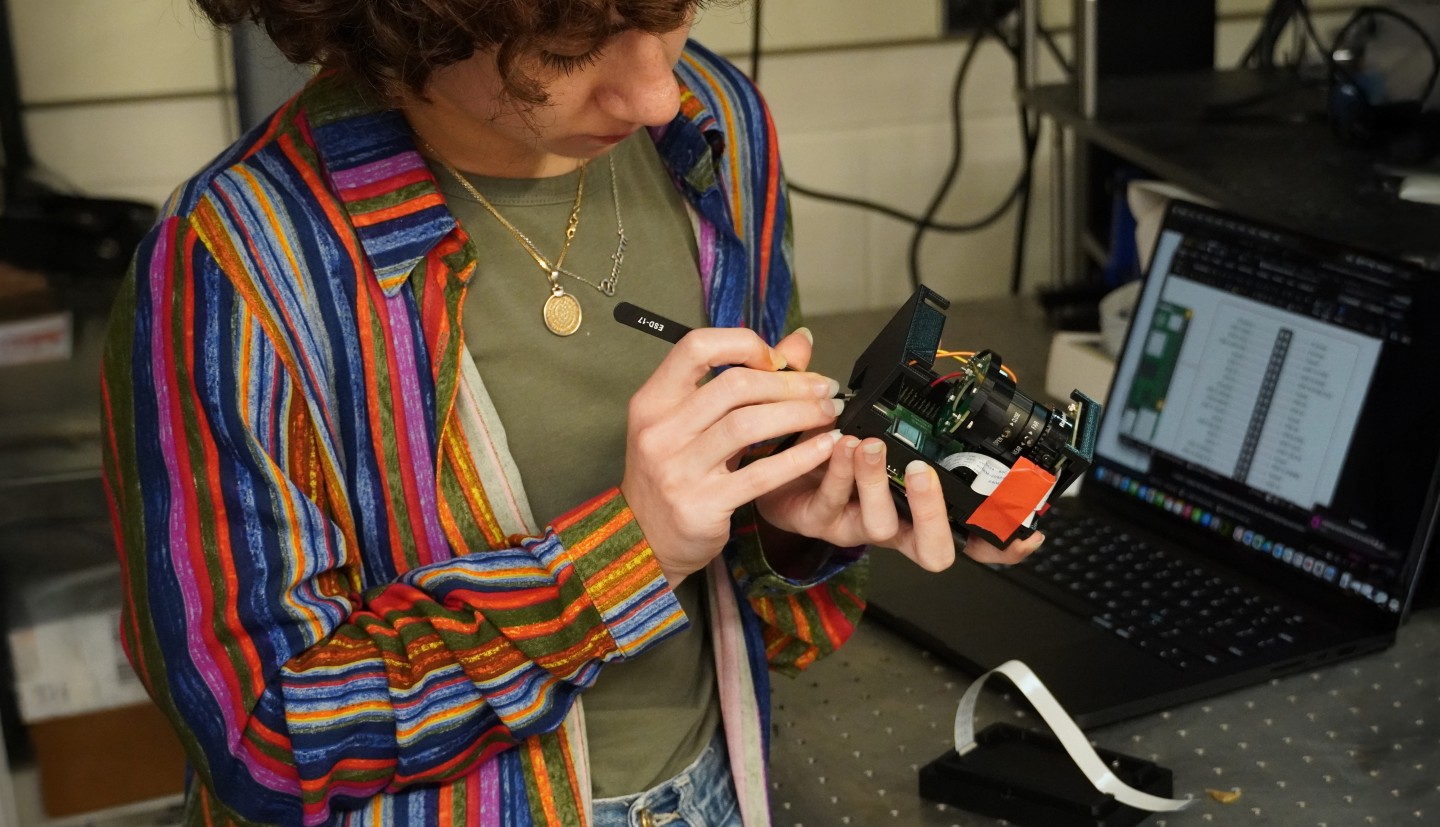 a woman holds piece of tech prototype in one hand works on it with tweezers