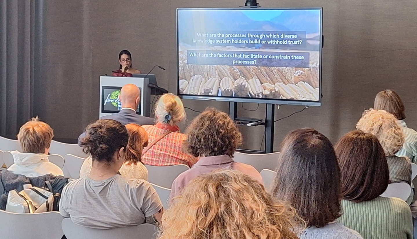 A woman presenting a lecture on a TV with a room of people