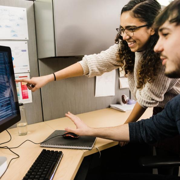 A young woman and a young man point at numbers on a computer screen