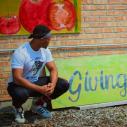 Student stands in front of a "Giving Garden" mural