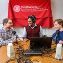 Students sit with podcast equipment in front of a Cornell Engineering flag
