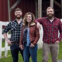 two young men and young woman stand outside of a barn