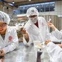 Male and female students in white lab jackets and hair nets standing around a metal table testing ice cream