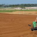 A man wearing a hat uses a piece of John Deer farm equipment in an open field