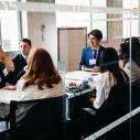 Male and female students sitting in a room at a table talking to one another