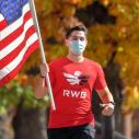A man running outside while holding an American flag and wearing a mask