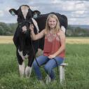 Rachel sitting on a stool outside holding onto a cow's bridal
